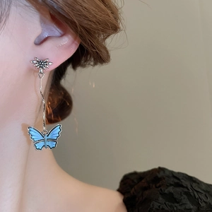Close-up of blue butterfly drop earrings with silver flower studs on a model