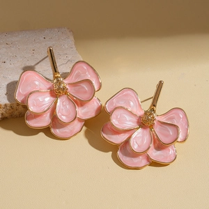 Macro detail of pink ginkgo leaf flower earrings with gold edges on a warm stone