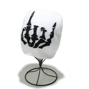 Detail of white knit beanie with black skeletal hand embroidery on a metal stand