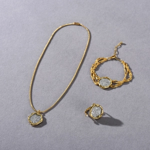 Flat lay of vintage gold-plated coin necklace, bracelet, and pearl ring set on grey