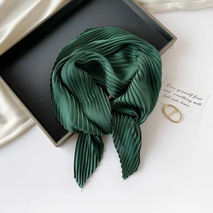 Detail of a green pleated silk scarf neatly knotted in a black tray for styling