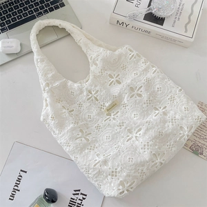 Close-up of the delicate floral lace embroidery and gold logo plate on the tote bag