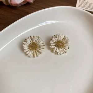 Detail view of raffia daisy earrings on a white ceramic plate with a wooden background