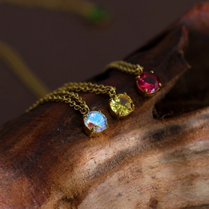 Three dainty birthstone necklaces with colorful crystals on a textured wooden background