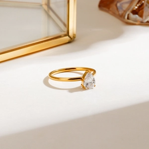 Detailed view of a gold teardrop cz ring with three-prong setting on a luxury surface