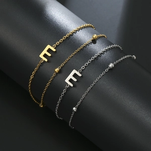 Macro shot of gold and silver letter E chain bracelets on a black display stand