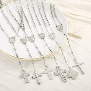 Set of six stainless steel rosary necklaces with cross pendants on a white ceramic tray
