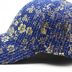 Macro shot of navy blue tweed baseball cap with intricate gold flower print detailing