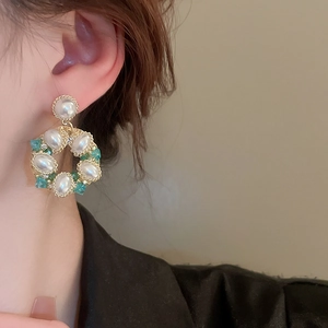 Close-up of vintage flower earrings with pearls and green crystals on a model