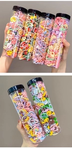 Detail showing four round plastic tubes filled with colorful elastic hair ties for kids