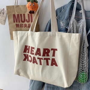 Detail of off-white canvas tote bag featuring bold red HEART ATTACK lettering in a lifestyle setting