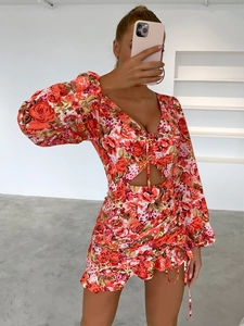 Détail de robe rouge fleurie à manches longues, col en V, taille évidée et ourlet volanté