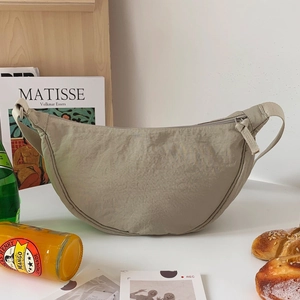 Minimalist beige nylon crescent crossbody bag with adjustable strap on white table