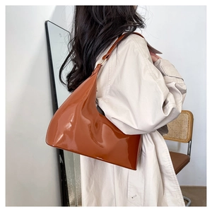 Close-up of glossy brown patent leather shoulder bag with sleek minimalist curved design