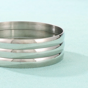 Close-up of three stacked minimalist polished silver stainless steel rings on blue surface