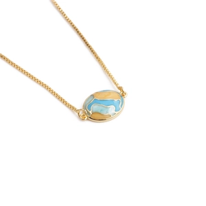 Detail view of a gold chain necklace with a blue and beige enamel oval pendant