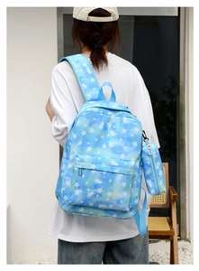 Rear view of model wearing a light blue tie-dye backpack with white stars and matching pouch