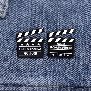Detail of movie clapperboard enamel pins with film quotes on blue denim fabric