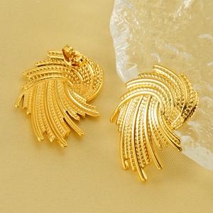 Golden irregular swirl earrings with textured wheat-ear pattern on a beige fabric background