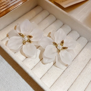 Close-up of white resin flower earrings with frosted petals and gold pearl stamens