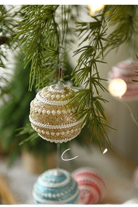 Close-up of pearl-embedded Christmas ball with glitter on a lit tree branch
