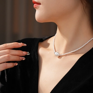Dettaglio di elegante collana di perle con perla centrale su modella in abito di velluto nero
