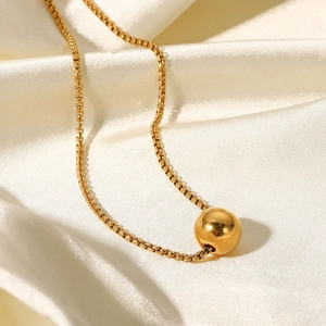 Macro view of gold ball pendant on box chain over elegant white silk background