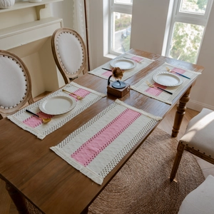 Detail of pink and beige woven cotton placemats with fringe on a wooden table