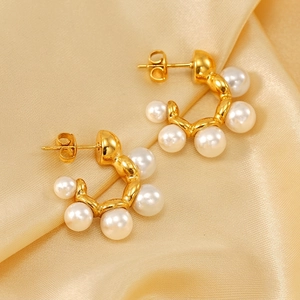 Elegant gold C-shaped hoop earrings with pearls on soft gold satin fabric background