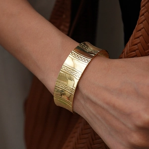 Vue macro d'un bracelet manchette doré avec des rayures verticales et des textures grainées