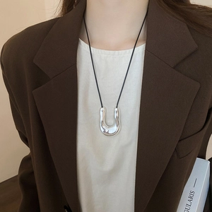 Detail of silver U-shaped organic liquid pendant on black cord worn with a brown blazer