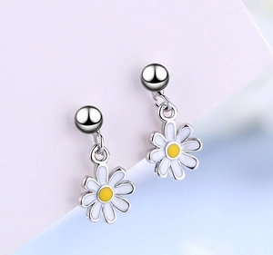 Macro shot of daisy stud earrings with white enamel petals and yellow center on pink card