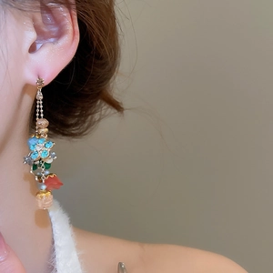 Close-up of beaded flower drop earrings with blue crystals and pearls worn by a model