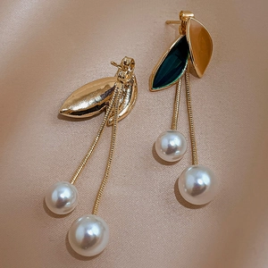 Close-up of pearl tassel earrings with green and amber leaves on warm satin