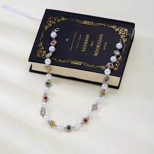 Detail of a pearl necklace with colorful rhinestone flowers on a vintage notebook