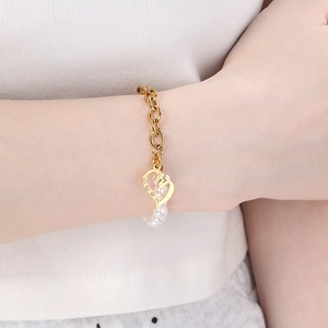 Detail of gold heart pendant with zircon and pearl on a titanium steel chain bracelet