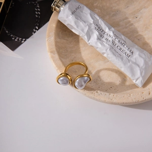 Close-up of golden adjustable ring with dual baroque pearls on a textured stone tray