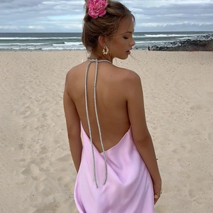 Robe dos nu en satin rose avec chaînes en strass présentée sur une plage ensoleillée