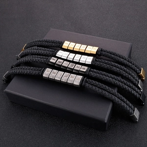 Detail of men's woven leather bracelets featuring engraved metallic slider charms