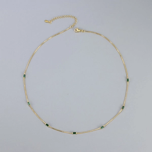 Elegant gold chain necklace featuring emerald green zircon stones on neutral background