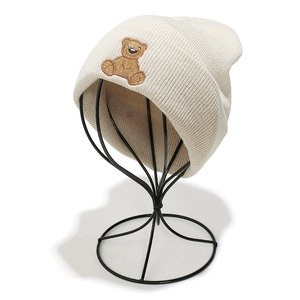 Detailed view of cream knitted beanie featuring a brown embroidered sitting bear motif