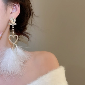 Macro view of crystal heart earrings with long feather tassels on a female model