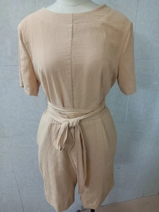 Détail d'une combinaison courte en coton lin beige avec ceinture nouée à la taille