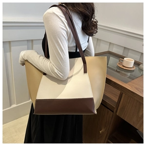 Side view of a large color-block tote bag in brown and beige leather on female model