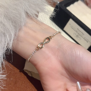 Detailed macro view of an infinity charm bracelet with micro-set zircons in golden finish