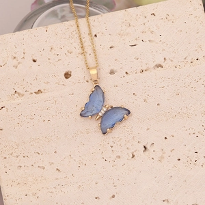 Macro d'un pendentif papillon bleu doré avec diamants posé sur un support en pierre