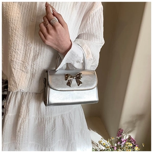Dettaglio della mini borsa argento con fiocco in pelle lucida e decoro metallico