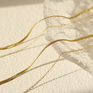 Detail von goldener Schlangenkette und feiner Gliederkette auf einer Glasplatte