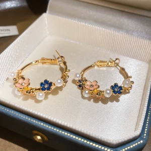 Macro detail of gold-plated hoop earrings with blue pink enamel flowers and pearls