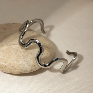 Detailed close-up of a wavy silver stainless steel open bangle on a natural stone base